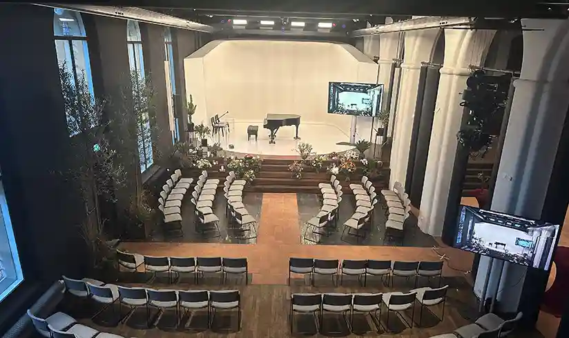 Een grote zaal met rijen stoelen en een zwarte piano op het podium